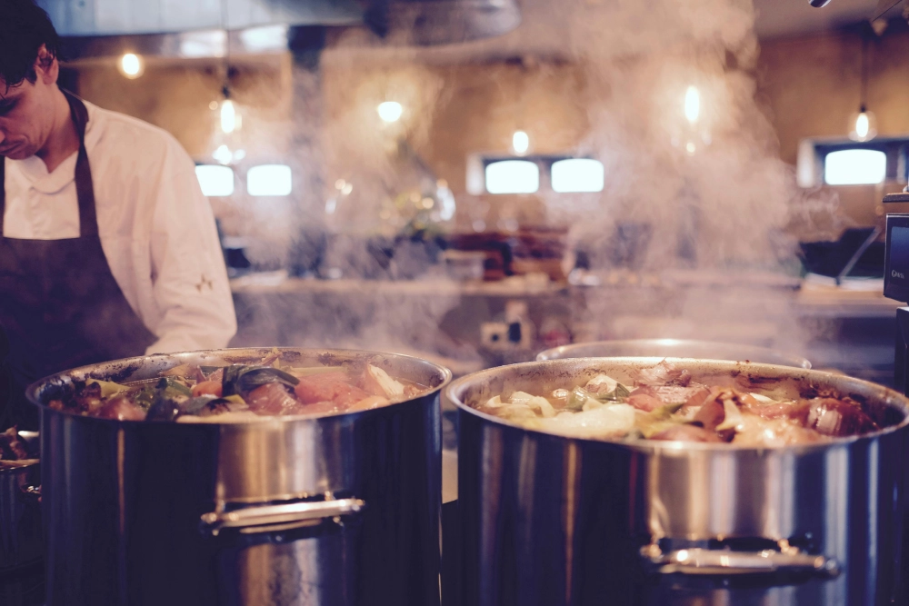 A chef is cooking in large pots on the stove.