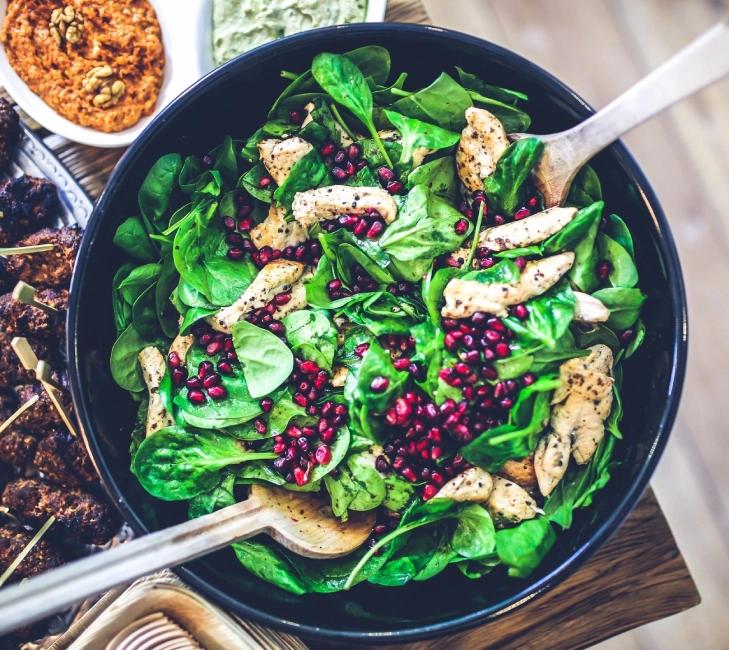 A bowl of salad with pomegranate seeds and chicken.