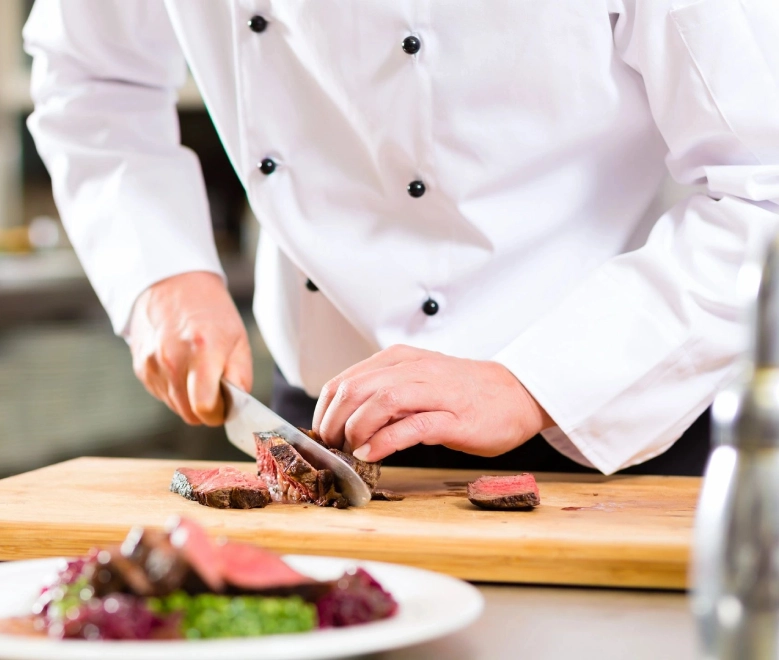 A chef cutting meat on top of a wooden board.