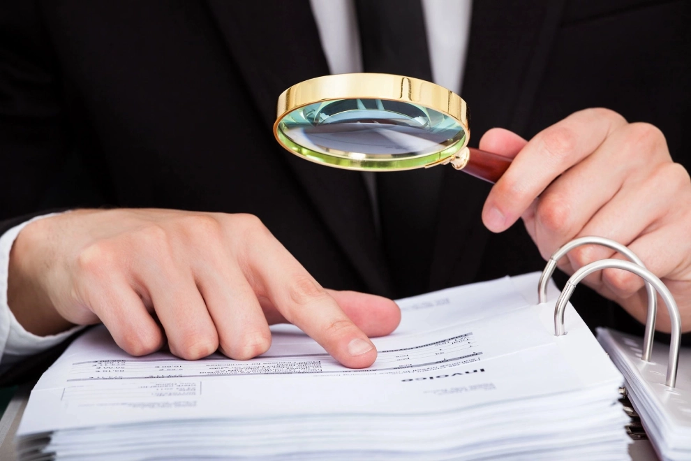 A person with a magnifying glass looking at papers