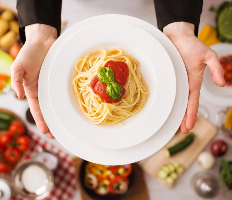 A person holding a plate of spaghetti with basil on it.