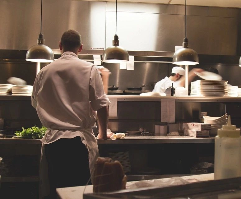 A man standing in front of two other men working at a restaurant.