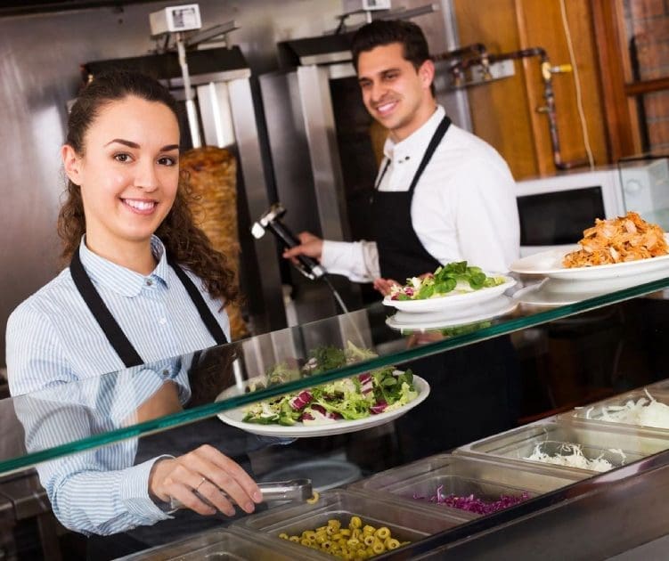 Two people in aprons serving food at a restaurant.