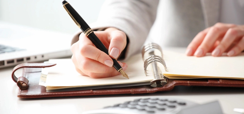 A person writing on paper with pen and calculator.