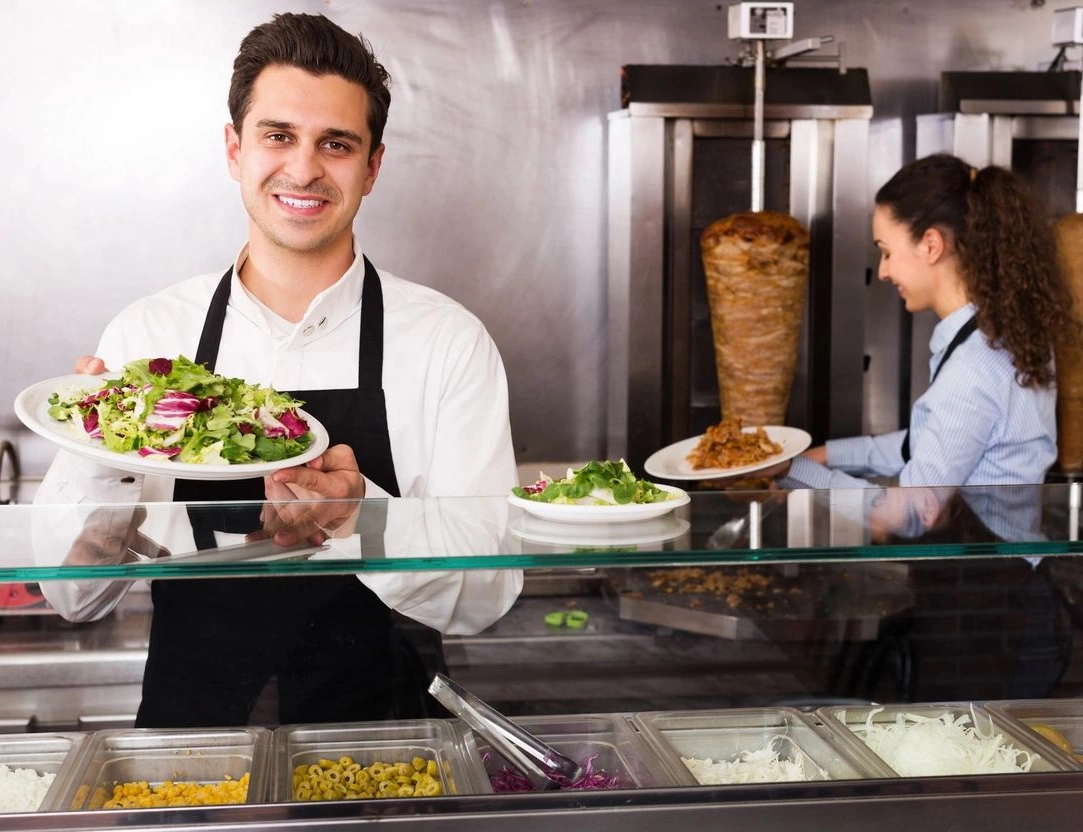 A man holding a plate of food behind a counter.