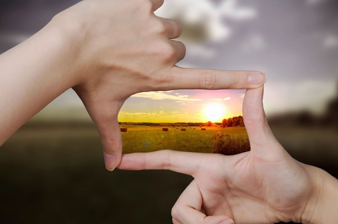 Hands framing a sunset over a field.